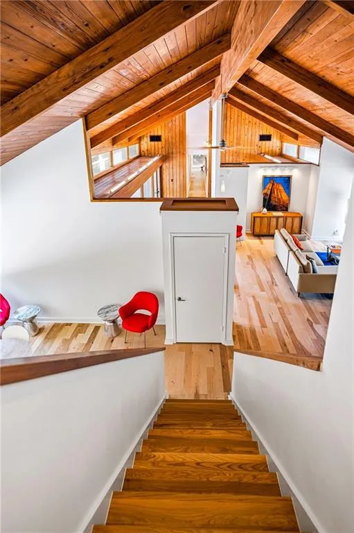 Vaulted wood-paneled ceilings with exposed beams, hardwood flooring throughout, and a prominent staircase featuring wood treads and white risers