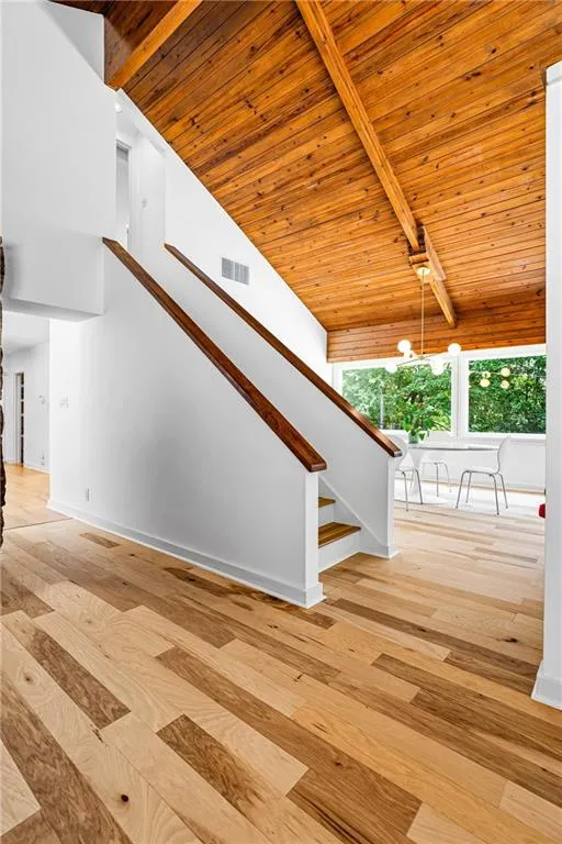 Hardwood flooring throughout the main level featuring a wood-finish vaulted ceiling with exposed beams, a partial staircase with wood handrails, and a dedicated dining area with large windows