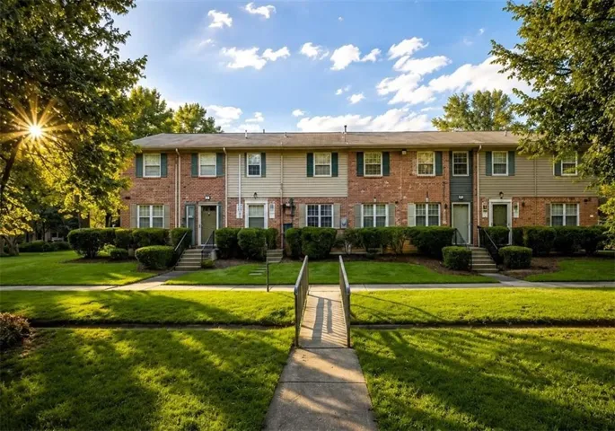 Brick and siding exterior with dark shutters, front entryways with exterior lighting, concrete walkways, and landscaped shrubbery