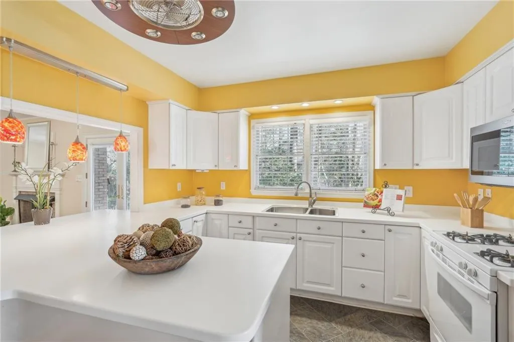 Kitchen featuring sink, white cabinets, decorative light fixtures, and white gas range