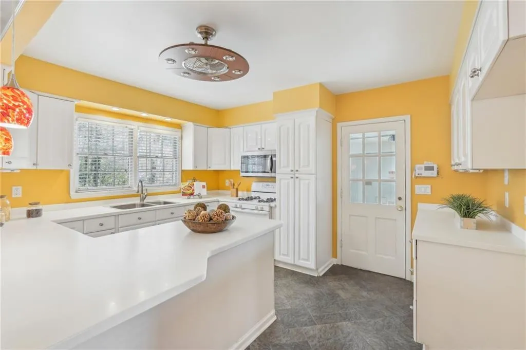 Kitchen featuring kitchen peninsula, decorative light fixtures, gas range gas stove, sink, and white cabinets