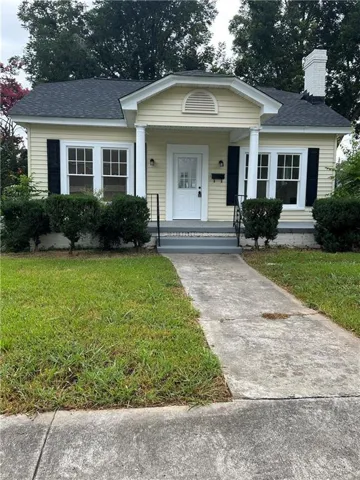 Yellow siding exterior featuring a covered porch with white columns, a black asphalt shingle roof, and a white brick chimney
