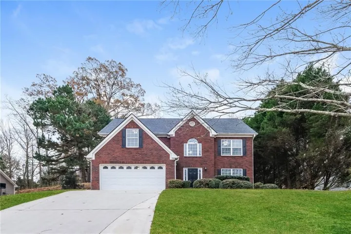 View of front of house with driveway, brick siding, a front yard, and roof with shingles