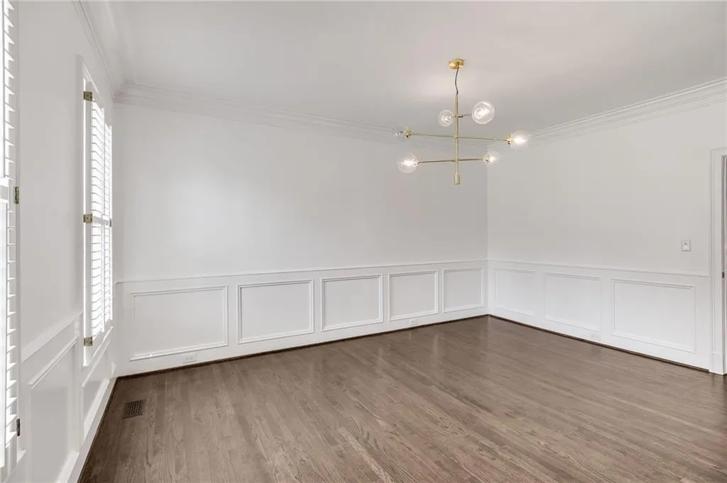 Unfurnished dining area with crown molding, dark wood-style floors, a decorative wall, wainscoting, and a chandelier