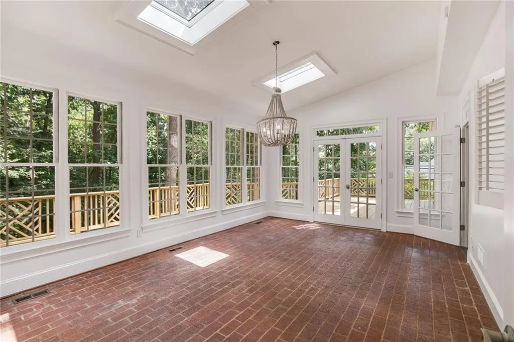 Unfurnished sunroom with a skylight, french doors, vaulted ceiling, brick flooring, and a chandelier