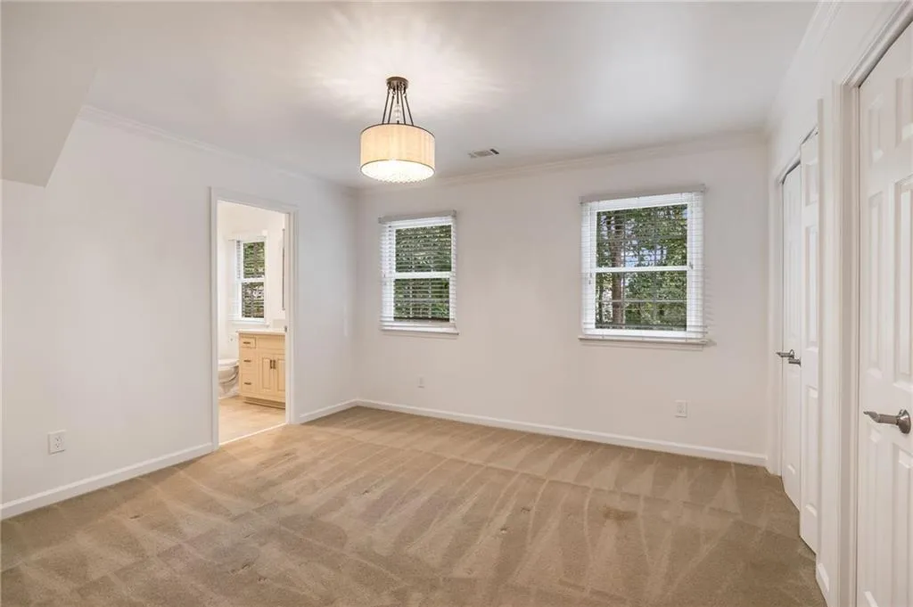 Unfurnished bedroom featuring ornamental molding, light colored carpet, ensuite bathroom, and a closet