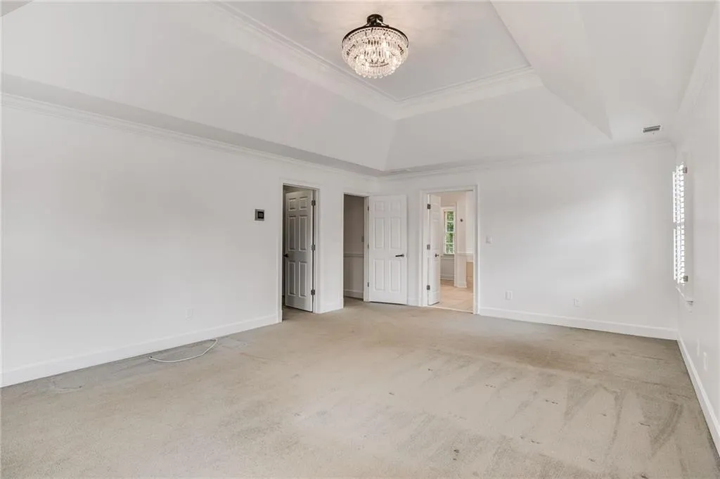Unfurnished bedroom with a raised ceiling, light carpet, ornamental molding, a chandelier, and ensuite bathroom