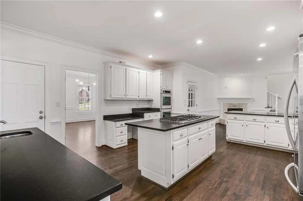 Kitchen with dark wood finished floors, ornamental molding, a center island, white cabinetry, and appliances with stainless steel finishes
