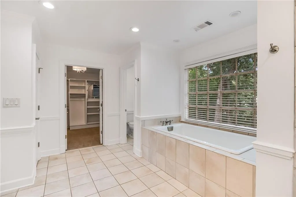 Bathroom featuring a bath, light tile patterned flooring, crown molding, a walk in closet, and recessed lighting