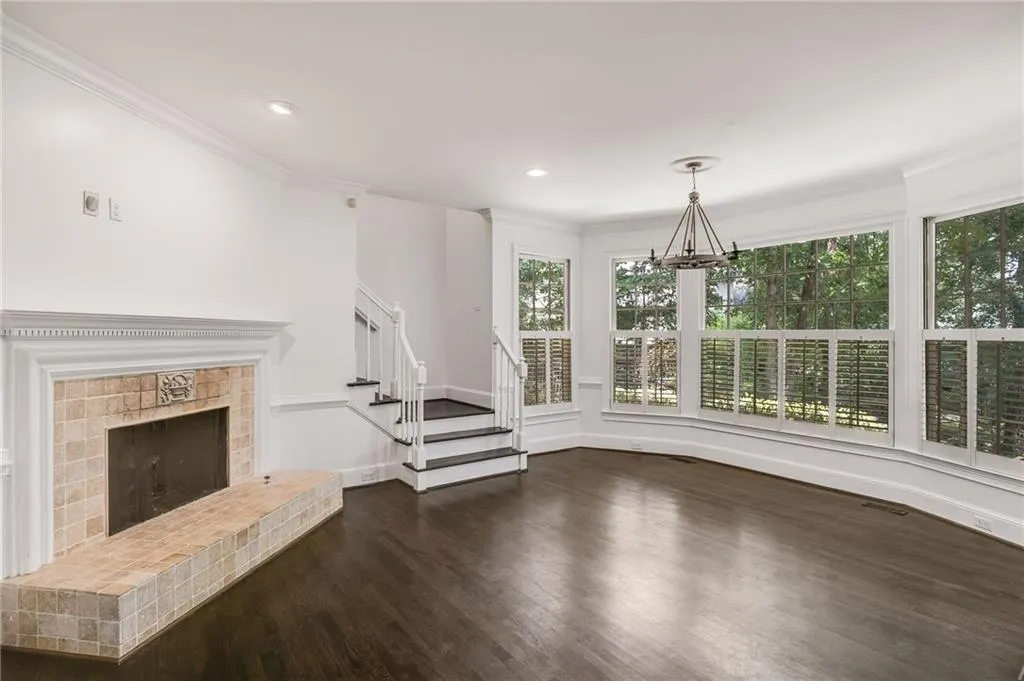 Unfurnished living room featuring dark wood-type flooring, a fireplace with raised hearth, crown molding, a chandelier, and stairs