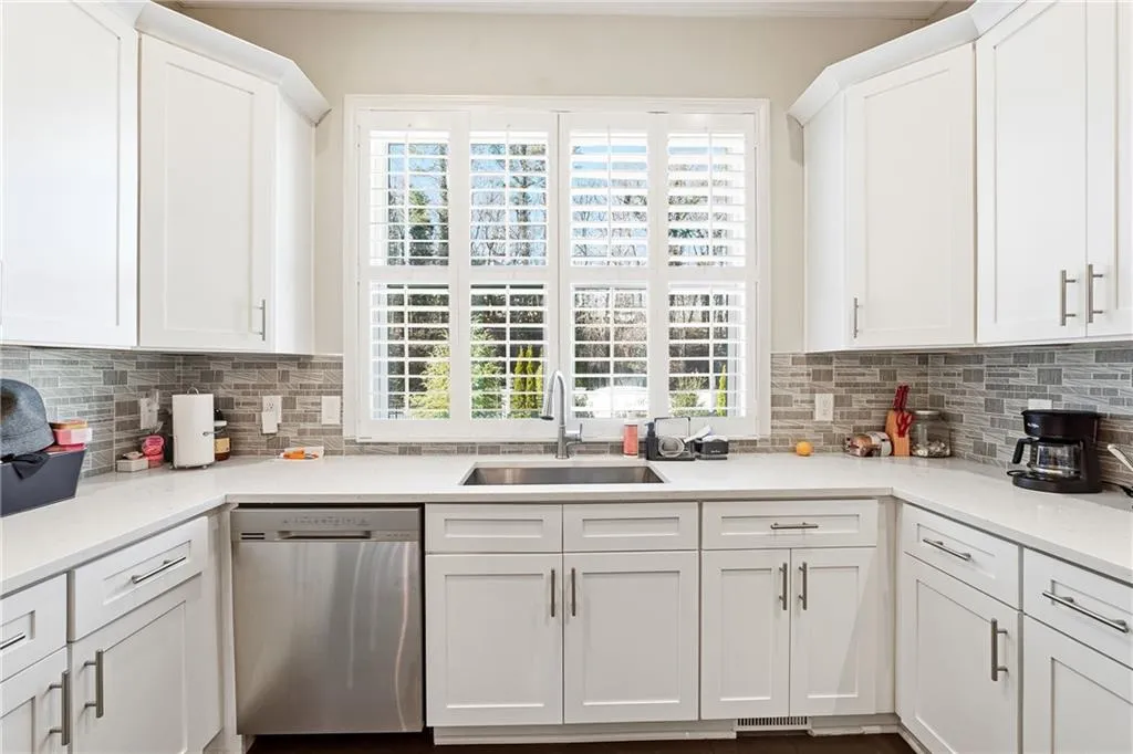Kitchen featuring white cabinets, dishwasher, decorative backsplash, and light stone counters