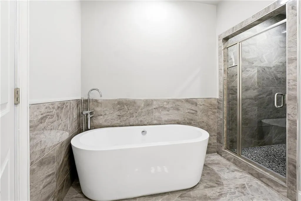 Bathroom featuring tile walls, a wainscoted wall, a stall shower, and a soaking tub