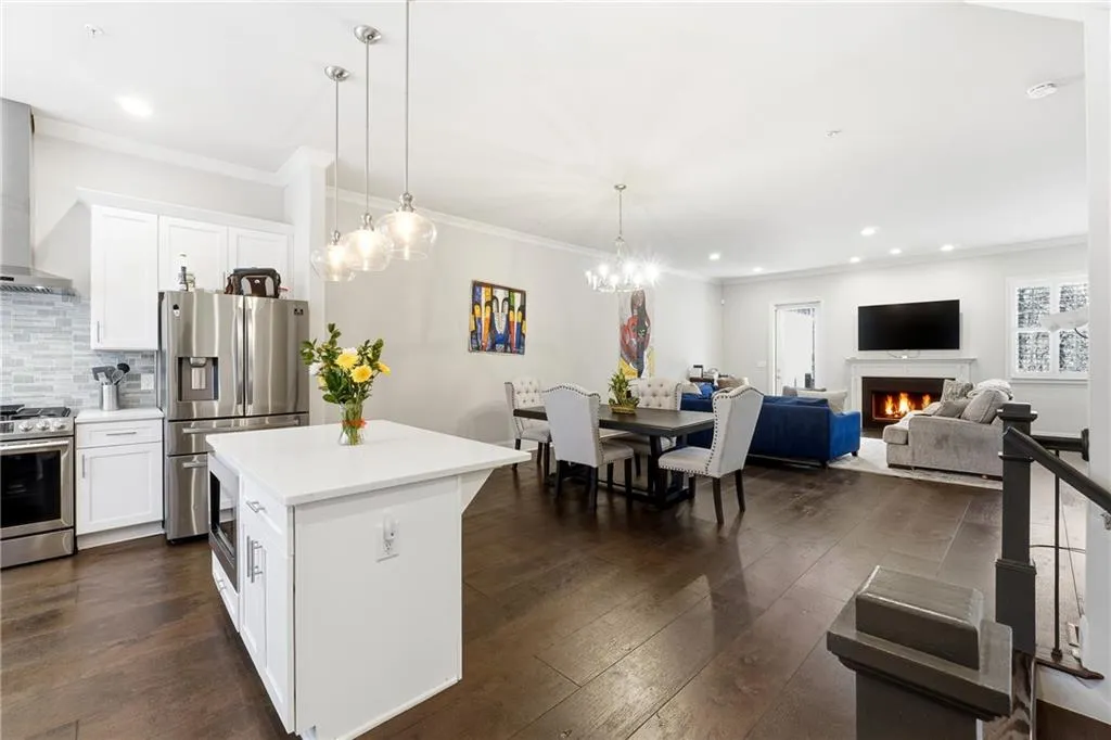 Kitchen featuring white cabinetry, open floor plan, appliances with stainless steel finishes, pendant lighting, and a warm lit fireplace