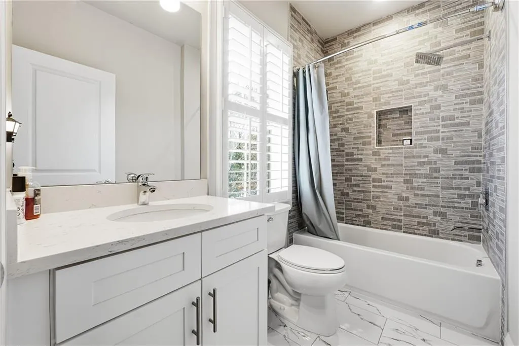 Bathroom featuring vanity, shower / bath combo, and marble look tile flooring