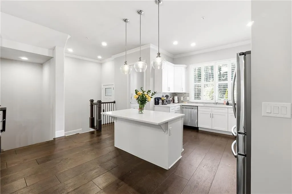 Kitchen with white cabinetry, dark wood-style flooring, stainless steel appliances, hanging light fixtures, and tasteful backsplash