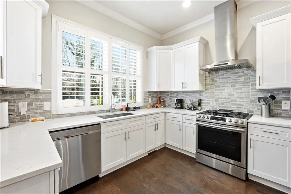 Kitchen with appliances with stainless steel finishes, wall chimney range hood, white cabinetry, crown molding, and tasteful backsplash