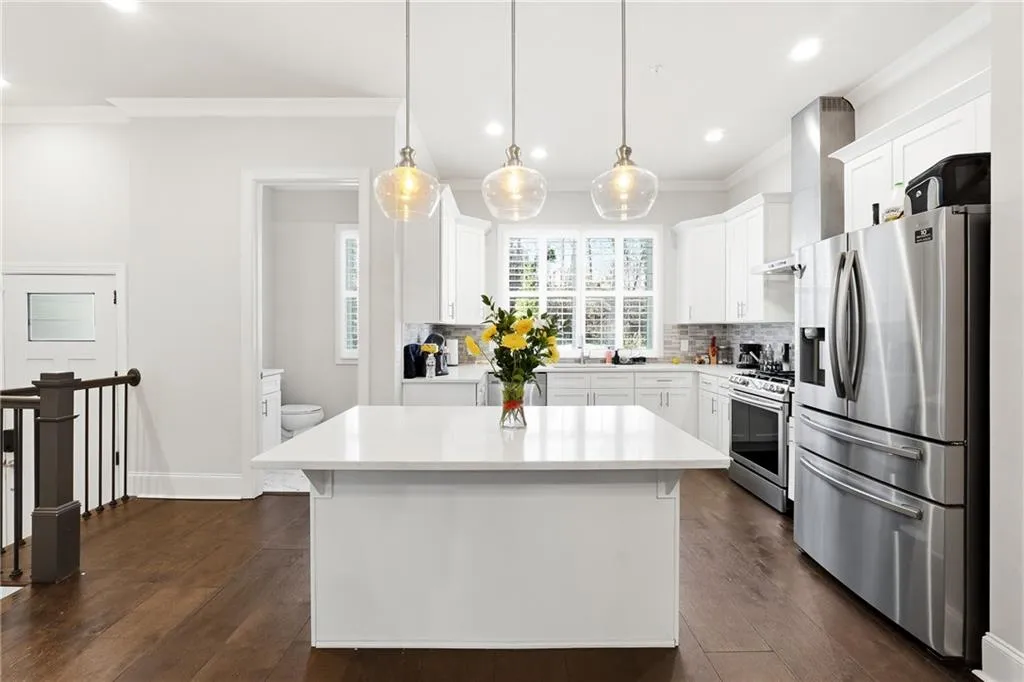 Kitchen with stainless steel appliances, ornamental molding, white cabinets, a center island, and dark wood-style flooring
