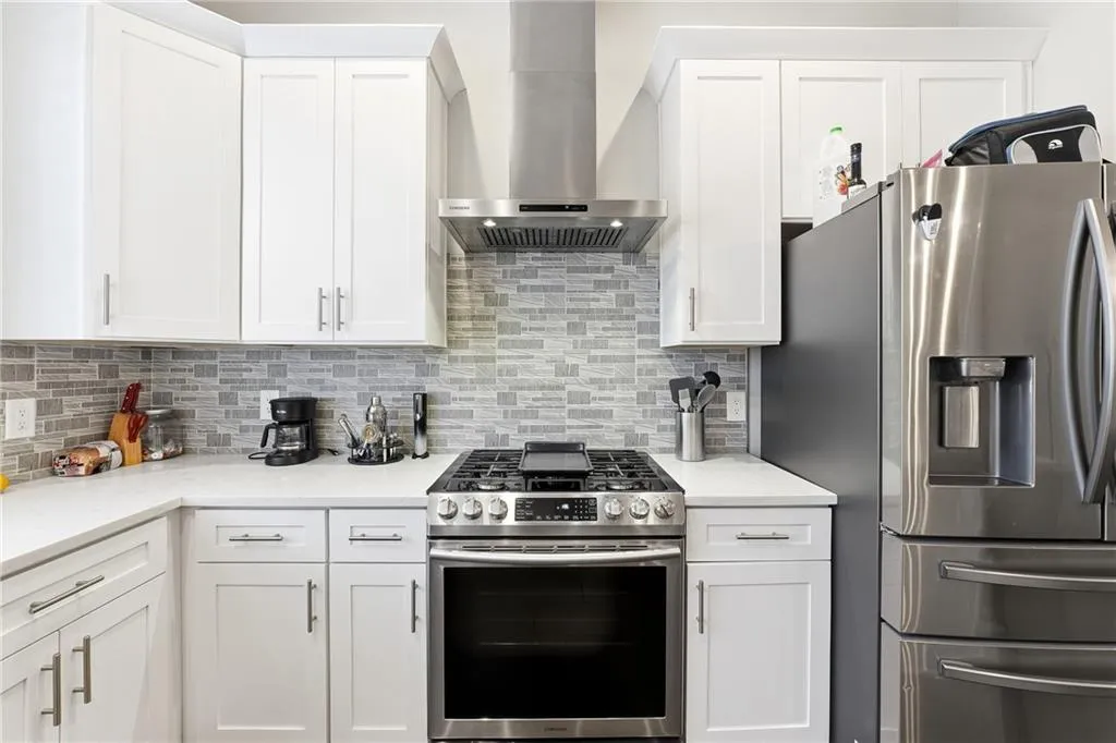 Kitchen with stainless steel appliances, white cabinets, wall chimney range hood, and light stone counters