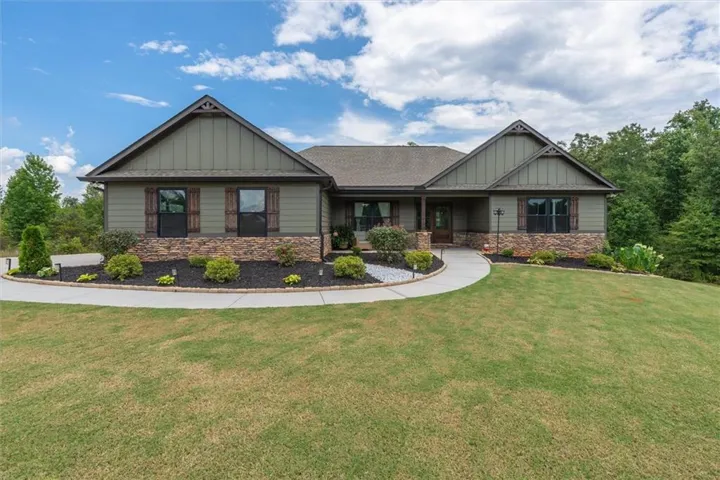 Gable roofline, stone veneer detailing, wood-finish window shutters, curved concrete pathway, and landscaped beds with ground cover
