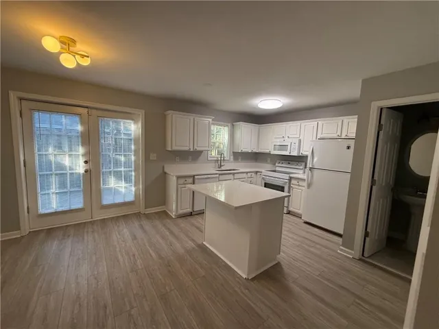 Kitchen featuring wood-finish flooring, white cabinetry, a central island, and white appliances