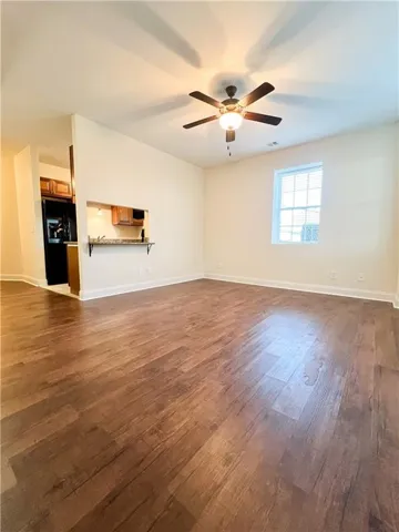 Unfurnished living room featuring ceiling fan, baseboards, and dark wood-type flooring