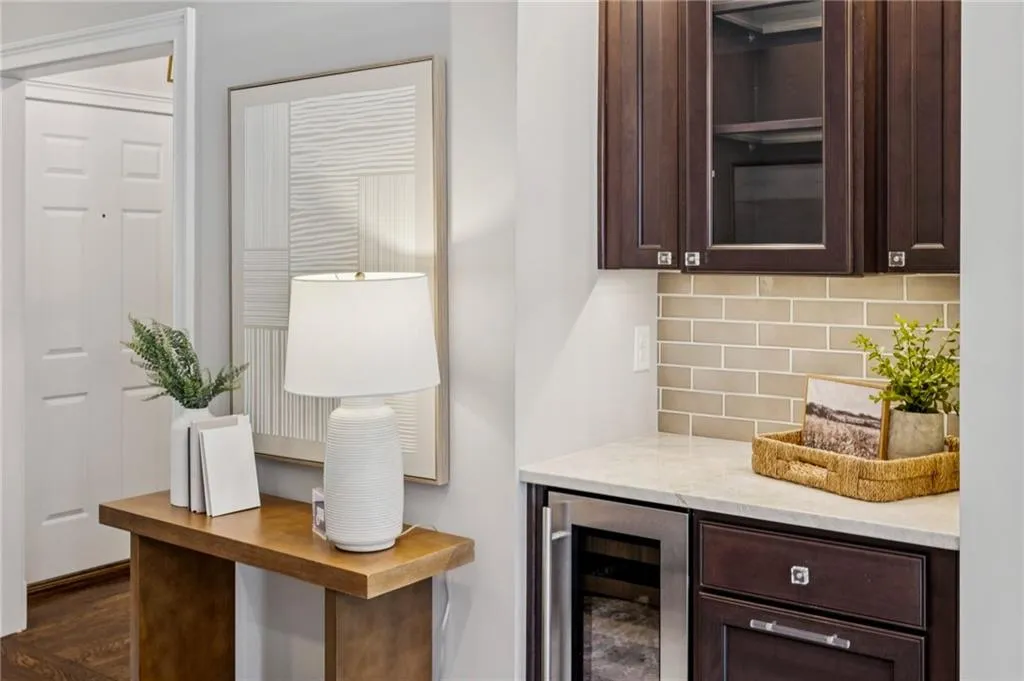 Bar area featuring dark brown cabinets, light stone countertops, beverage cooler, tasteful backsplash, and glass insert cabinets