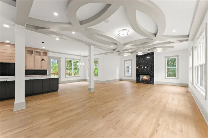 Spacious open-concept interior featuring light wood-finish flooring, an elaborate tray ceiling design with recessed lighting, and a contemporary fireplace with a black marble-style surround