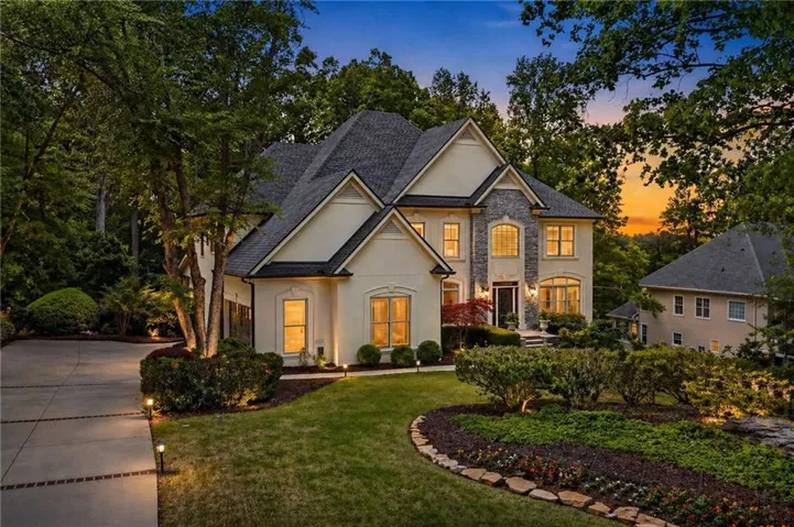 Stucco and stone exterior with a multi-gabled roofline, complemented by a landscaped lawn with mature trees and a paved driveway