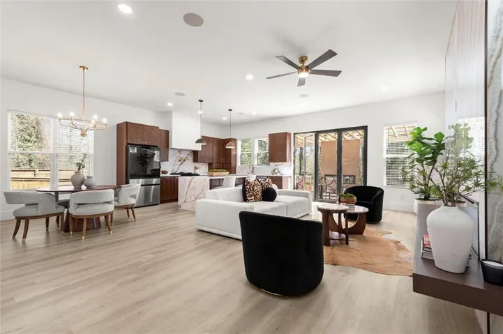 Open-concept living area with wood-finish flooring, a modern kitchen, a dining area with a chandelier, a living room with ceiling fan, and large glass doors leading to an outdoor space