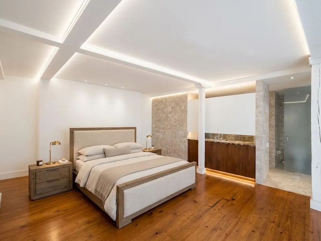Hardwood flooring throughout, coffered ceiling with recessed lighting, stone accent wall, integrated cabinetry, and an open concept bathroom area, virtual staging bedroom furniture and LED lighting