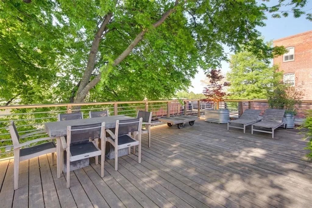 Expansive rooftop deck featuring wood-finish flooring, metal railing, and mature tree canopy