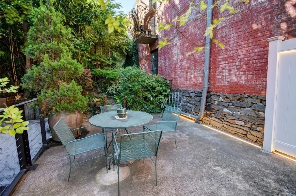 Private patio featuring a concrete surface, a brick exterior wall, a stone foundation, extensive perimeter landscaping, and integrated wall lighting