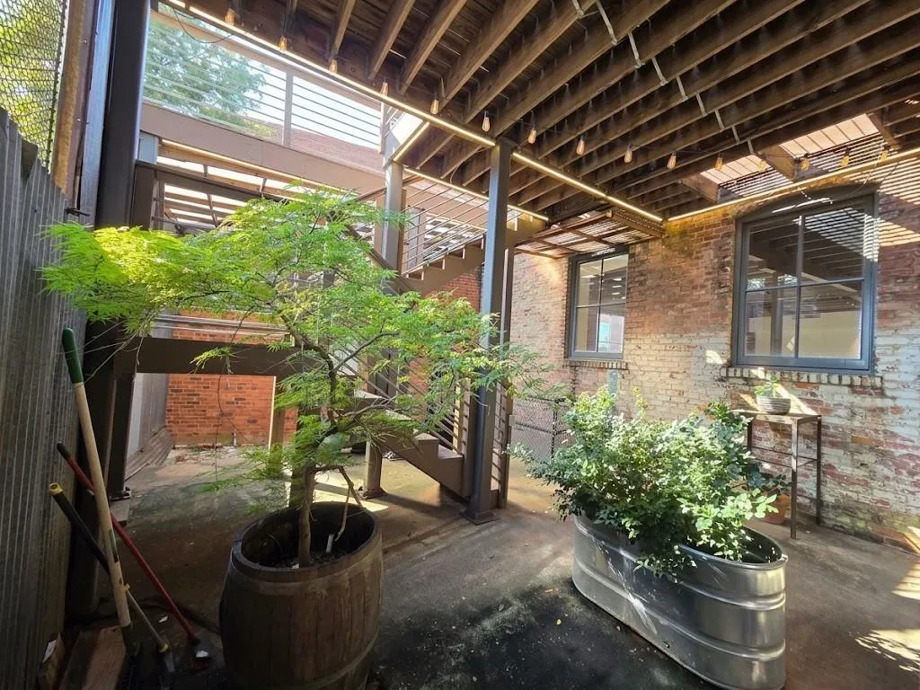Exposed brick exterior with multiple windows, concrete ground-level patio, and a slatted wood ceiling