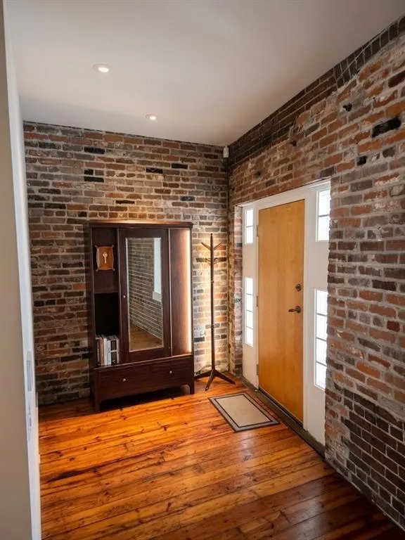 Exposed brick walls, wood-finish flooring, recessed ceiling lighting, natural wood door, and sidelight windows