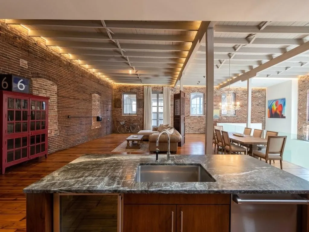 Exposed brick walls, wood-finish flooring, beam ceiling, recessed lighting, and a kitchen island with an undermount sink, virtual LED lighting and furniture