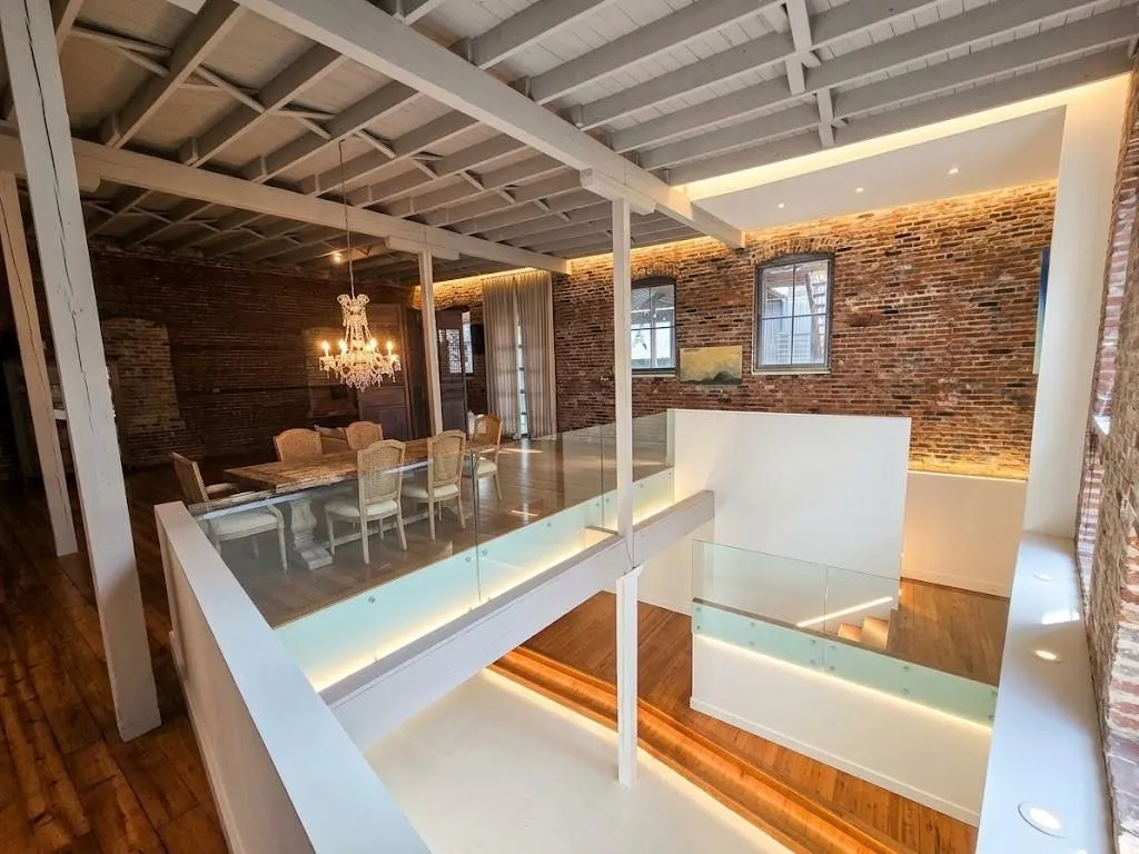 Exposed brick walls, wood-finish flooring, glass railings with integrated lighting, exposed ceiling beams, and a chandelier illuminate the space, virtual LED lighting