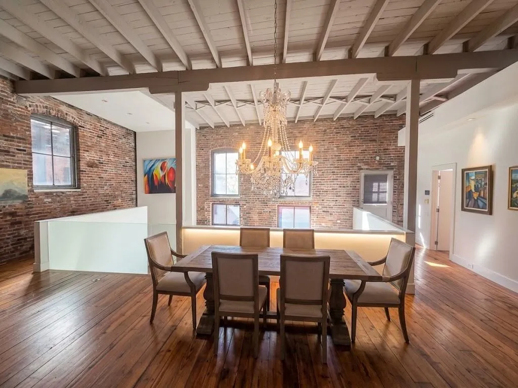 Open-concept dining area featuring exposed brick walls, wood-finish flooring, an exposed beam ceiling, and a crystal chandelier, virtual staging dining