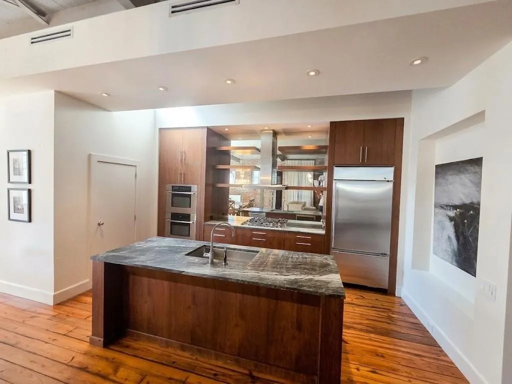 Gourmet kitchen featuring a built-in double oven, stainless steel appliances, a large center island with an undermount sink, rich wood cabinetry, and wood-finish flooring