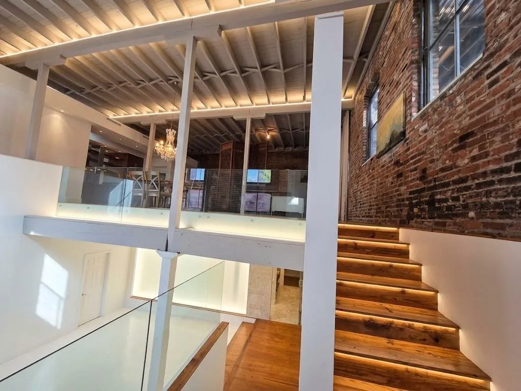 Exposed brick accent wall, wood tread stairs with integrated lighting, glass panel railings, open-beam ceiling, and wood-finish flooring, virtual LED lighting
