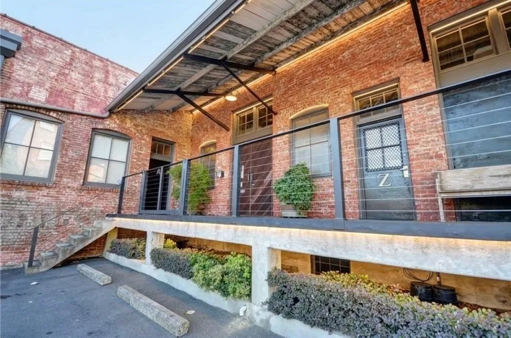 Exposed brick exterior with multiple window openings, a concrete and metal railing balcony, and integrated planter boxes with shrubbery