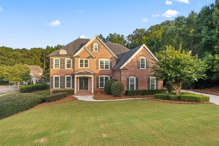 Traditional brick-front residence featuring a gabled roofline, multiple windows with dark shutters, and a covered entry