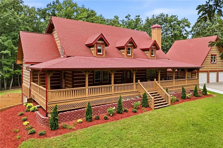 Log-style home featuring a red shingle roof, expansive wrap-around porch with natural wood railing, multiple dormer windows, and a three-car garage