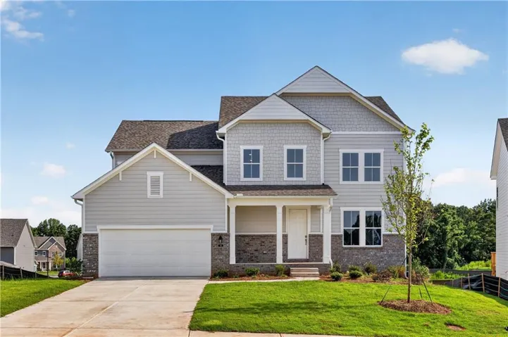 Two-story residence featuring light gray siding with shingle and horizontal paneling accents, a covered front porch, a two-car garage, and a concrete driveway