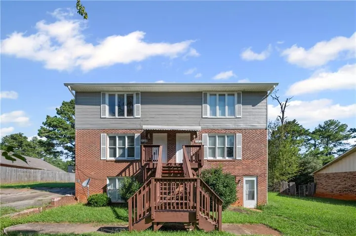 Brick and siding exterior featuring white window shutters, dual entry doors, and a central exterior staircase with wood railings