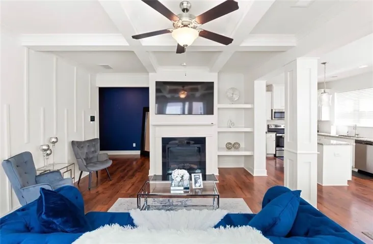 Living area featuring a coffered ceiling, wood-finish flooring, a built-in fireplace with a mantel, integrated shelving, and white wainscoting