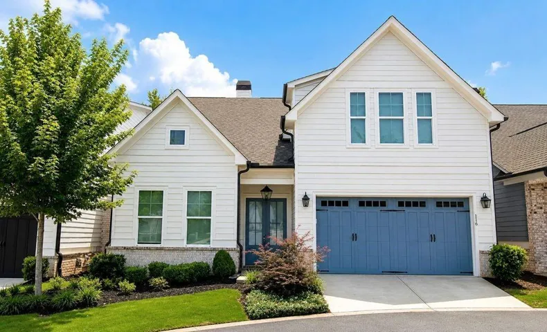 Contemporary farmhouse-style exterior featuring white siding, a prominent gable roofline, a blue garage door, dark trim details, and mature landscaping