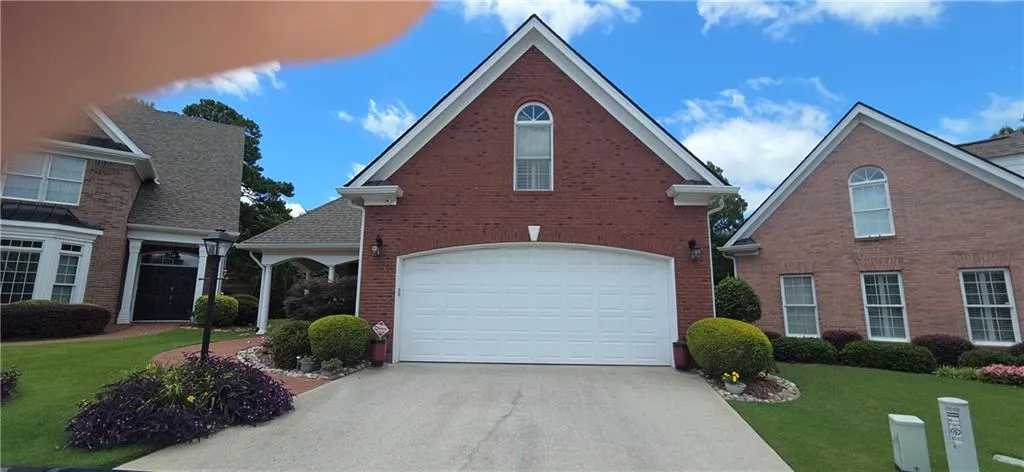 Brick exterior featuring a prominent garage with a white door, an arched window, and mature landscaping