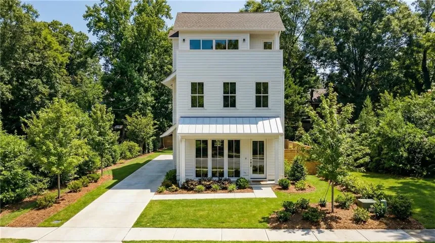 Three-story white siding exterior with a metal awning, featuring multiple large windows and a concrete driveway