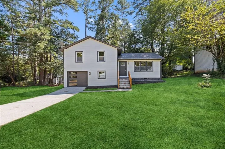 White siding exterior with a dark trim roof, attached garage with a frosted panel door, and concrete driveway