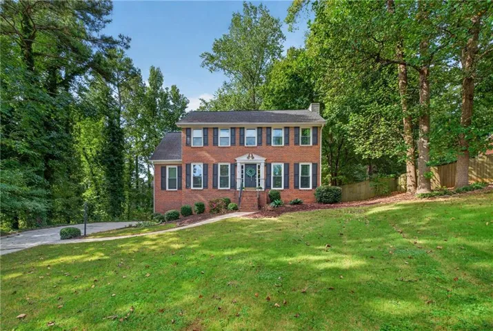 Two-story brick exterior with black shutters, concrete driveway, and established front landscaping